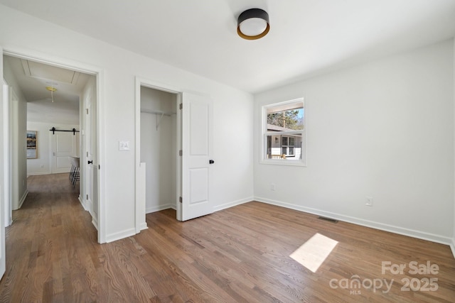 unfurnished bedroom with wood finished floors, visible vents, baseboards, a closet, and attic access