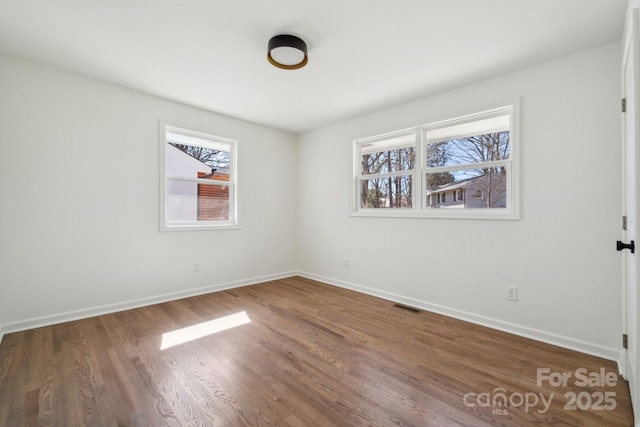 spare room with baseboards, visible vents, and wood finished floors