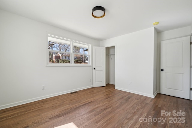 unfurnished bedroom featuring a closet, wood finished floors, visible vents, and baseboards