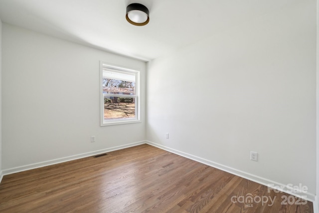 empty room with baseboards, visible vents, and wood finished floors