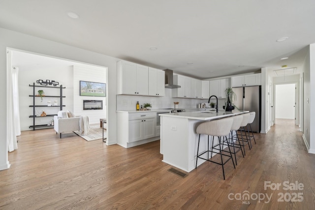 kitchen featuring a breakfast bar, visible vents, freestanding refrigerator, a sink, and wall chimney exhaust hood