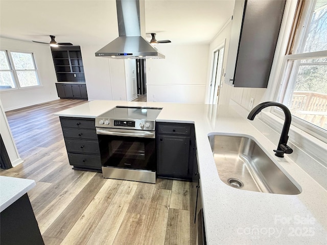 kitchen with stainless steel electric range oven, wall chimney exhaust hood, a peninsula, light wood-style floors, and a sink