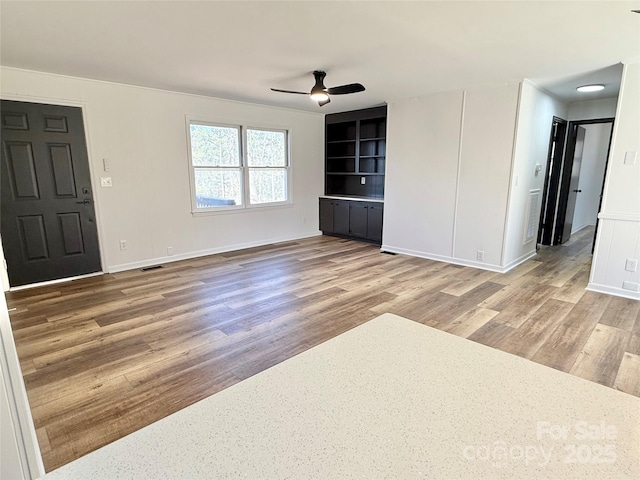 unfurnished living room with ceiling fan, wood finished floors, visible vents, and baseboards