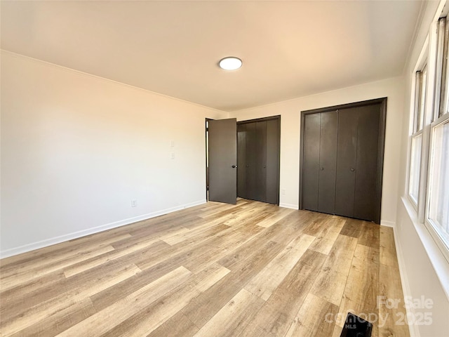 unfurnished bedroom with light wood finished floors, multiple windows, two closets, and baseboards