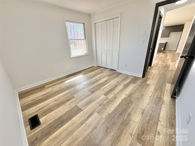 unfurnished bedroom featuring baseboards, ornamental molding, a closet, and light wood-style floors