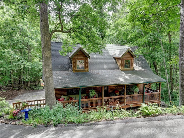 log-style house with covered porch, roof with shingles, and a view of trees