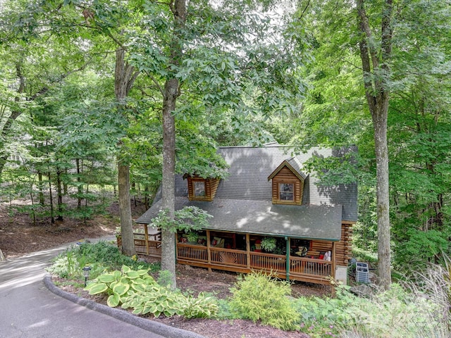 view of front of home with a shingled roof, a view of trees, log exterior, and a wooden deck