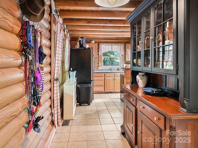 kitchen featuring rustic walls, glass insert cabinets, freestanding refrigerator, light tile patterned flooring, and a sink