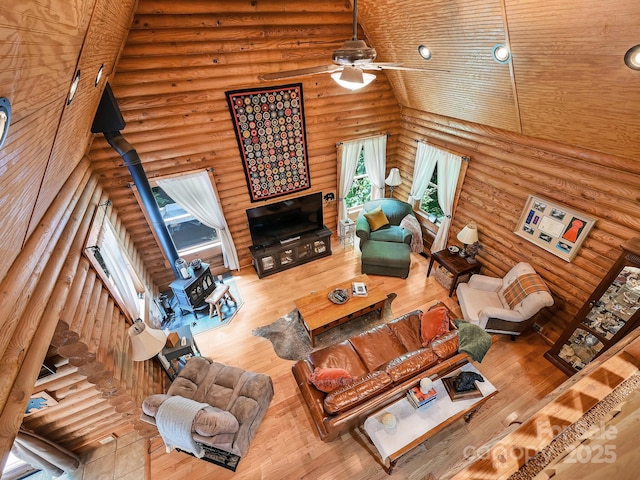 living area featuring high vaulted ceiling, hardwood / wood-style floors, a wood stove, and a ceiling fan