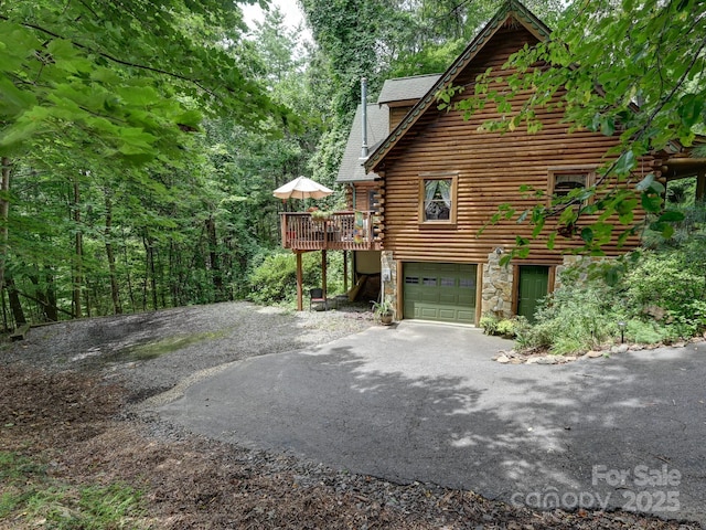 view of home's exterior with a deck, aphalt driveway, an attached garage, stone siding, and log exterior