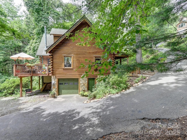 view of side of property featuring aphalt driveway, a garage, stone siding, a wooden deck, and log exterior