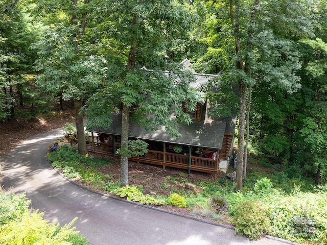 view of front of house with a shingled roof, a view of trees, and log exterior