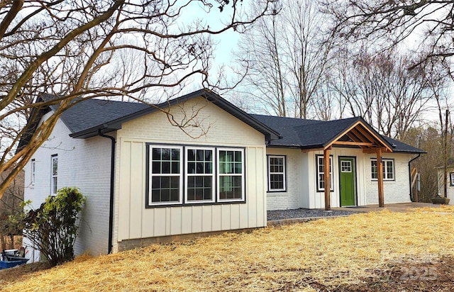 ranch-style house with a shingled roof, a front yard, brick siding, and board and batten siding