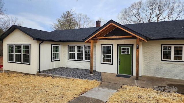 ranch-style home with a shingled roof, brick siding, and a chimney