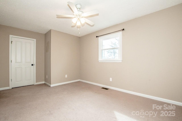 carpeted spare room featuring a ceiling fan, visible vents, and baseboards