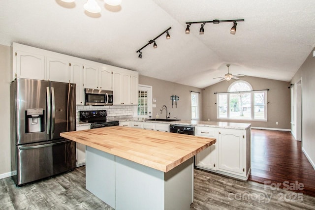 kitchen with wood counters, a peninsula, vaulted ceiling, black appliances, and a sink