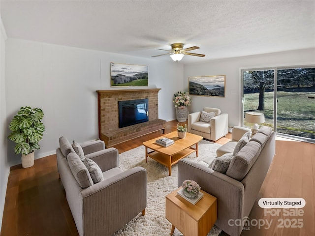 living area with a ceiling fan, a fireplace, a textured ceiling, and wood finished floors