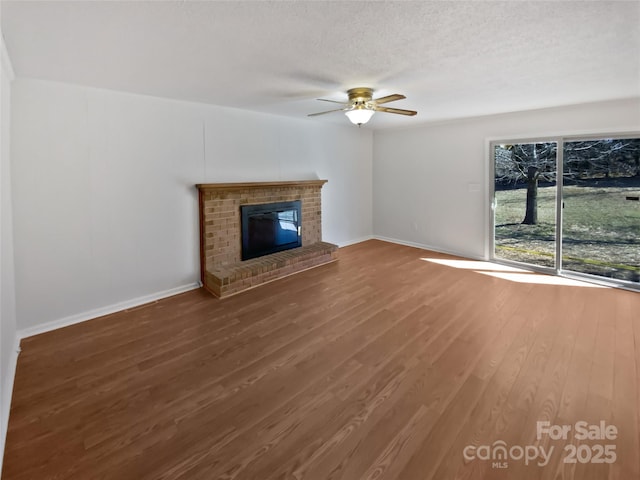 unfurnished living room with a textured ceiling, wood finished floors, a ceiling fan, baseboards, and a brick fireplace