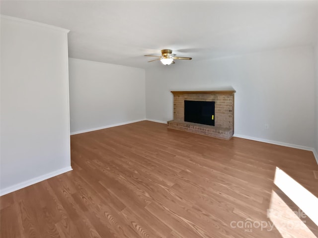 unfurnished living room with baseboards, a fireplace, a ceiling fan, and wood finished floors