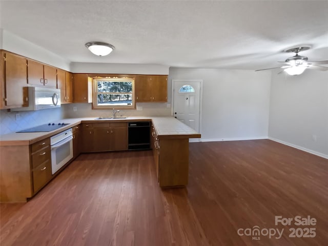 kitchen with black appliances, tile counters, brown cabinetry, and dark wood-type flooring