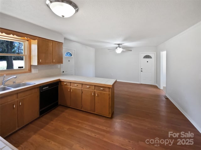 kitchen featuring a peninsula, a sink, black dishwasher, brown cabinetry, and dark wood finished floors