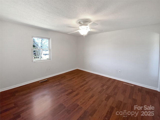 empty room with dark wood finished floors, visible vents, ceiling fan, a textured ceiling, and baseboards