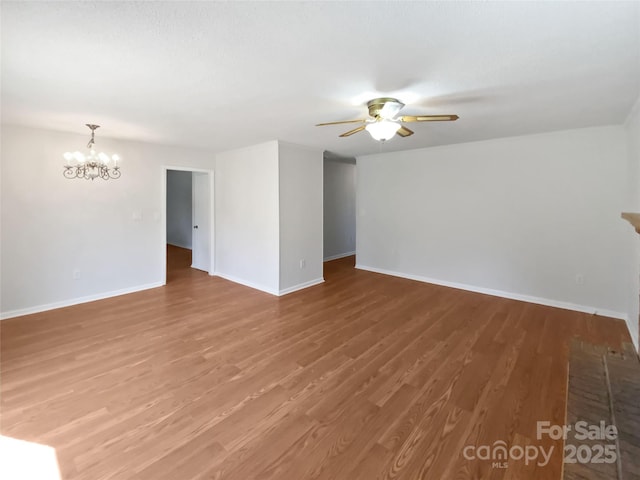 spare room featuring ceiling fan with notable chandelier, wood finished floors, and baseboards