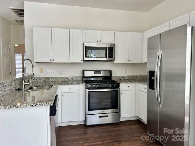 kitchen featuring white cabinets, appliances with stainless steel finishes, light stone counters, dark wood-type flooring, and a sink