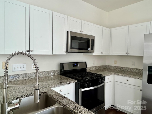 kitchen with light stone countertops, white cabinetry, appliances with stainless steel finishes, and a sink