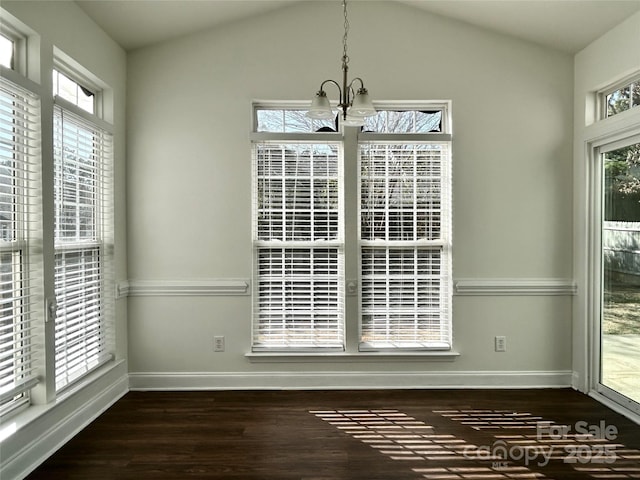 unfurnished dining area featuring an inviting chandelier, vaulted ceiling, baseboards, and wood finished floors