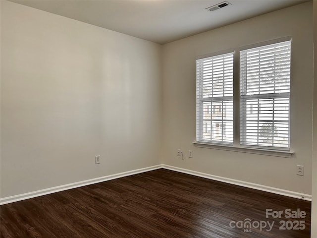 empty room featuring baseboards, visible vents, and dark wood-type flooring