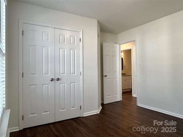 unfurnished bedroom with dark wood-type flooring, a closet, and baseboards