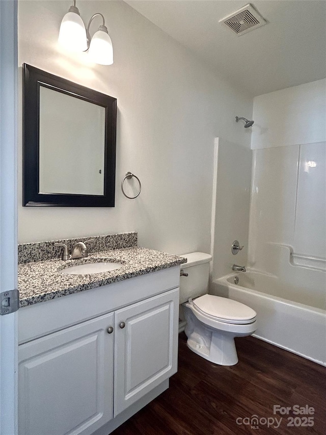 bathroom with toilet, wood finished floors, vanity, bathing tub / shower combination, and visible vents