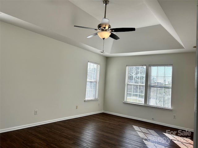 empty room with ceiling fan, baseboards, a raised ceiling, and dark wood-style flooring