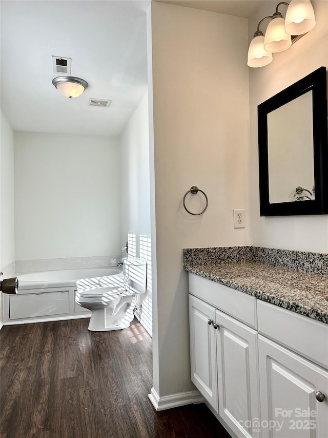 bathroom with visible vents, toilet, vanity, wood finished floors, and baseboards