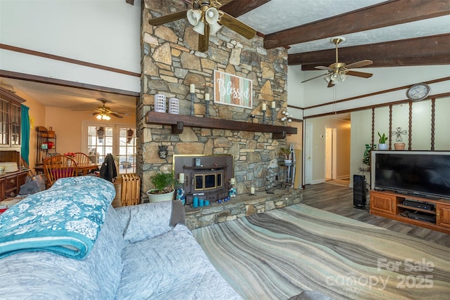 living area featuring a ceiling fan, a wood stove, and beamed ceiling