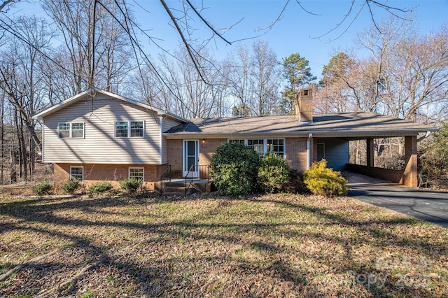 tri-level home with aphalt driveway, brick siding, a chimney, a front yard, and an attached carport