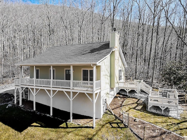 view of front of property featuring a shingled roof, a front yard, a chimney, and a wooded view