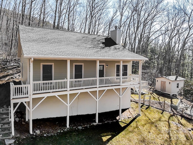 rear view of house featuring a shingled roof, a chimney, a shed, and an outdoor structure