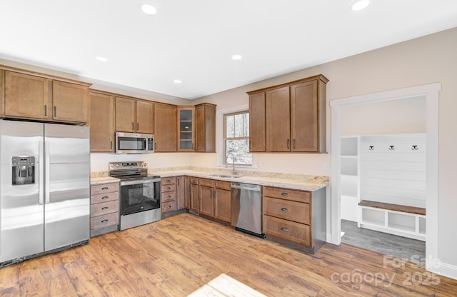 kitchen with recessed lighting, a sink, appliances with stainless steel finishes, light wood-type flooring, and brown cabinetry