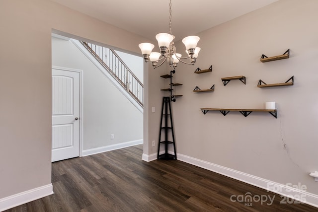 unfurnished dining area featuring dark wood-style floors, a chandelier, stairway, and baseboards