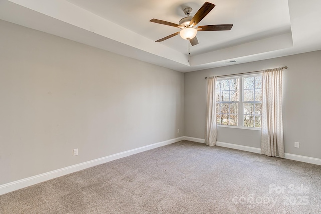 carpeted spare room with visible vents, baseboards, a raised ceiling, and a ceiling fan