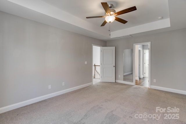 unfurnished bedroom featuring light colored carpet, a ceiling fan, visible vents, baseboards, and a raised ceiling