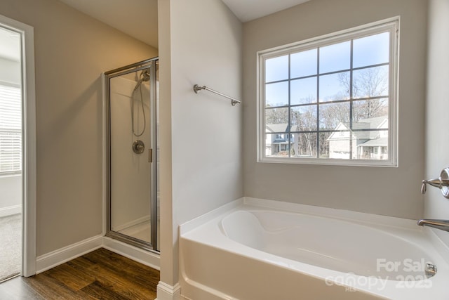 bathroom with a garden tub, wood finished floors, a shower stall, and baseboards