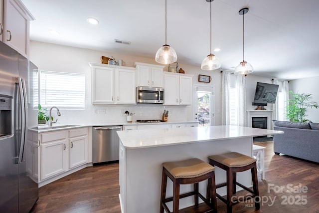 kitchen featuring stainless steel appliances, a sink, visible vents, backsplash, and dark wood-style floors