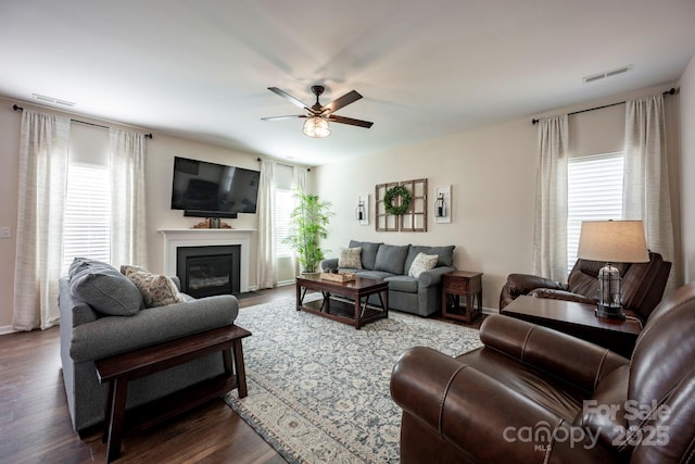 living area featuring dark wood-type flooring, visible vents, a fireplace with flush hearth, and a ceiling fan