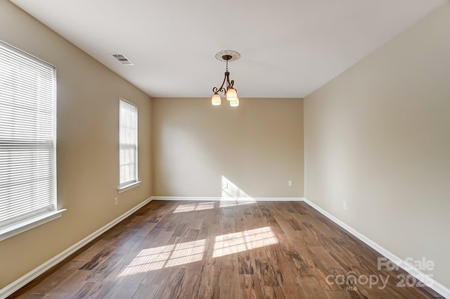 empty room with baseboards, visible vents, a chandelier, and wood finished floors