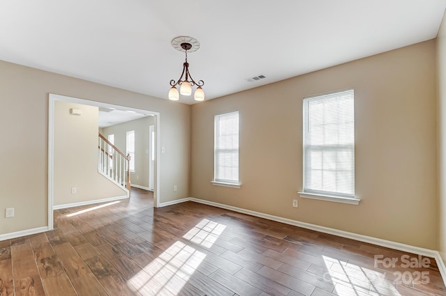 unfurnished room with a chandelier, wood finished floors, visible vents, baseboards, and stairs