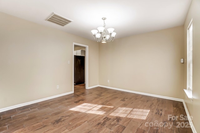 unfurnished room with a chandelier, wood finished floors, visible vents, and baseboards