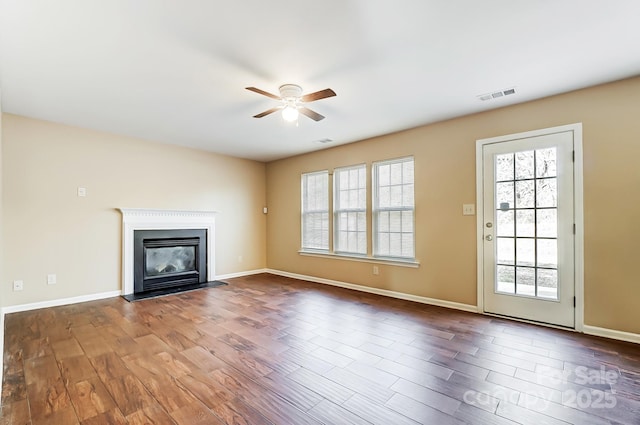 unfurnished living room with baseboards, visible vents, dark wood finished floors, a ceiling fan, and a glass covered fireplace